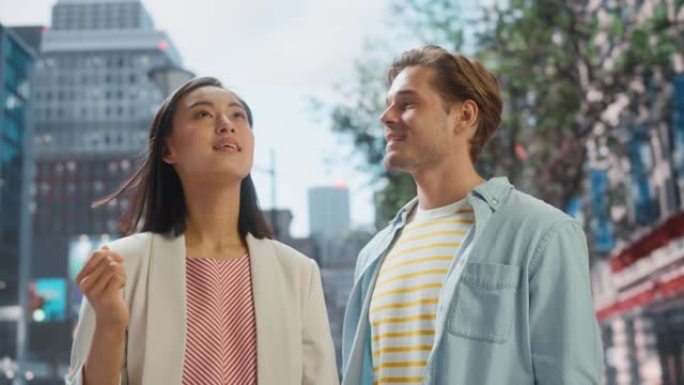 站在大城市街道上的一对年轻时尚多民族夫妇的肖像。迷人的日本女性和英俊的白人男性环顾四周。不同的朋友喜