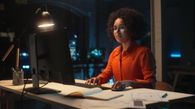 晚上在创意办公室的台式电脑上工作的年轻黑人女性。多民族营销经理写电子邮件，在线研究项目计划细节。
