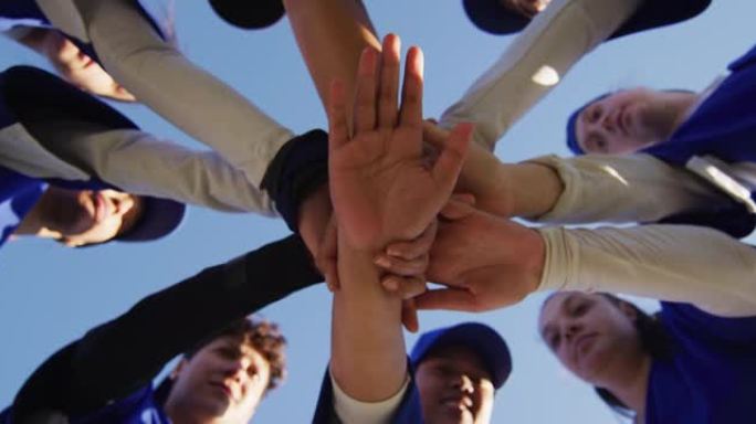 不同群体的女棒球运动员在蓝天下进行手工堆叠的低角度视图