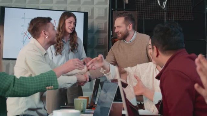 成功的商业交易快乐微笑的男女经理握手，在办公室慢动作与团队一起庆祝。