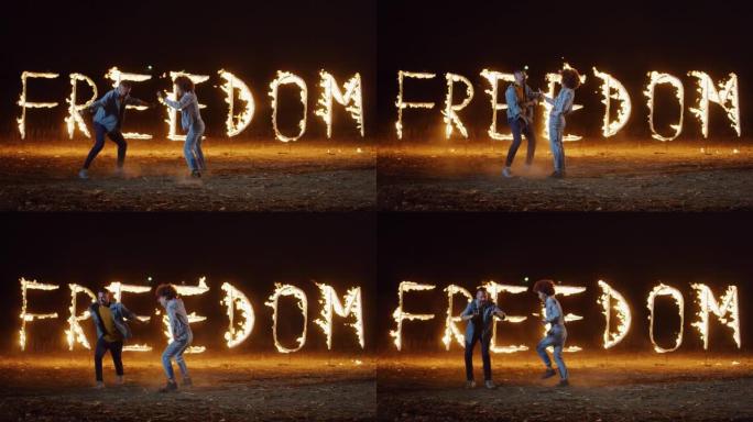 两个多民族年轻朋友的肖像在烟火火字母拼写自由的背景下跳舞。精力充沛的白人和非洲裔美国妇女庆祝他们的青