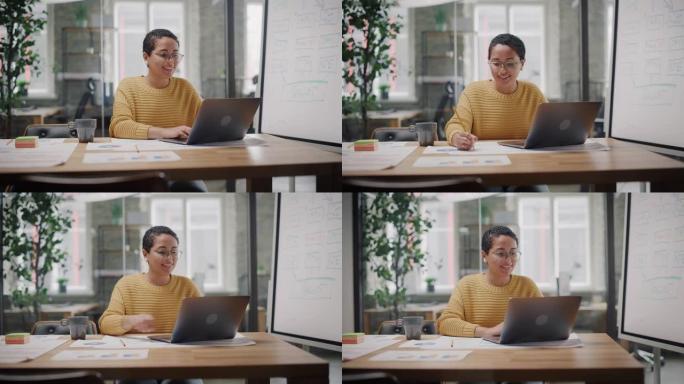 在繁忙的创意办公环境中，在笔记本电脑上工作的年轻拉丁营销专家眼镜肖像。美丽多样的多民族女性项目经理正