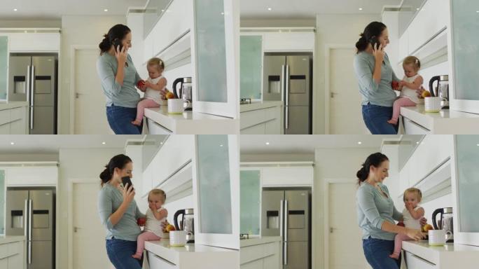 高加索母亲抱着婴儿在家里的厨房里用智能手机聊天
