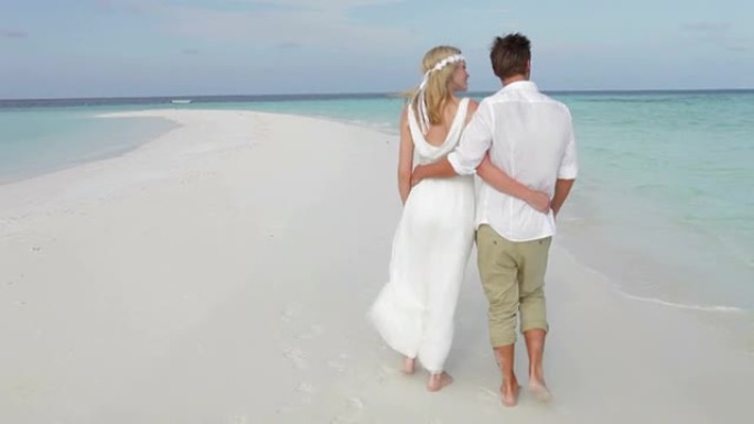 婚礼上沿着海滩散步的夫妇的后视图