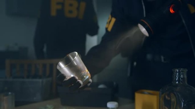 FBI探员在黑暗的公寓里拿着手电筒从厨房桌子上拿杯子