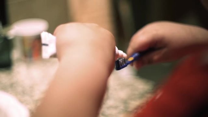 一个小男孩的手把牙膏放在浴室的牙刷上。特写。