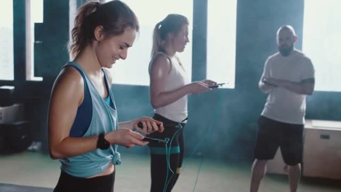 两名年轻快乐的运动白人女性在现代健身房跳绳锻炼前听个人男性健身教练。