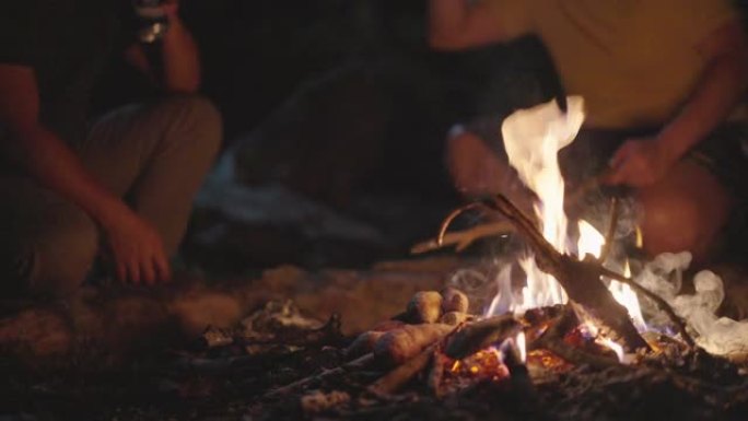 SLOMO两个男人手里拿着啤酒，在篝火中加入木头