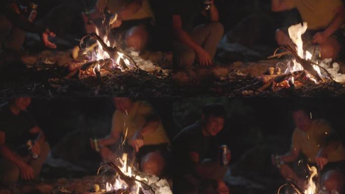 SLOMO两个男人手里拿着啤酒，在篝火中加入木头
