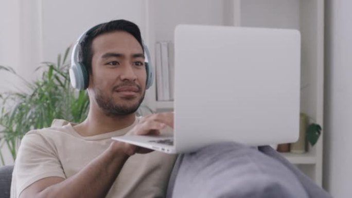音乐dj通过耳机在笔记本电脑上流式传输，同时在在线音乐订阅软件上混合新歌。微笑而放松的男人坐在家里的