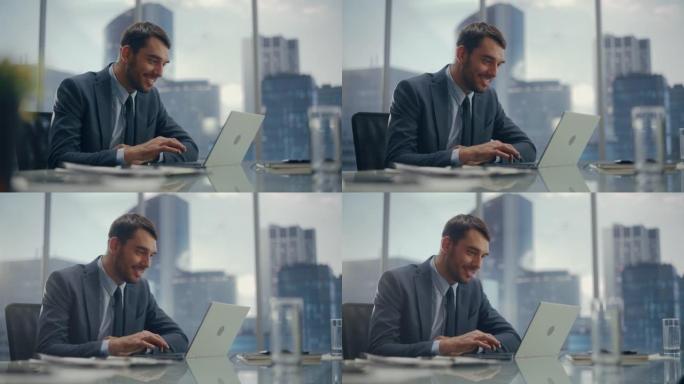 穿着西装的快乐商人坐在现代办公室的办公桌前，使用笔记本电脑，在窗户旁边，可以看到摩天大楼。成功的财务