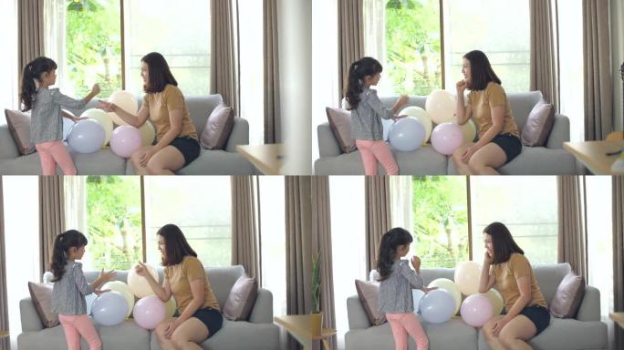 妈妈和可爱的小女孩女儿在家客厅沙发上玩气球