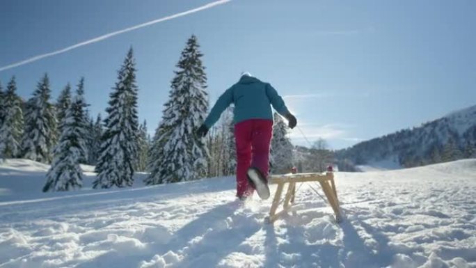 低角度: 面目全非的女人带着木制雪橇跑上雪山。