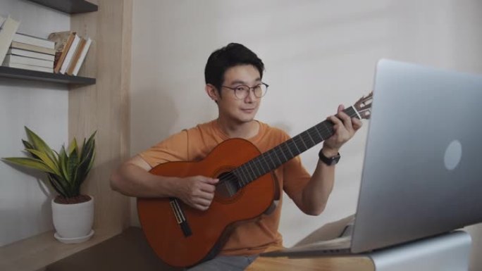 通过互联网上的视频通话，与他的朋友一起用音乐演奏吉他电话会议。玩古典吉他的人很开心。音乐家男子与他的