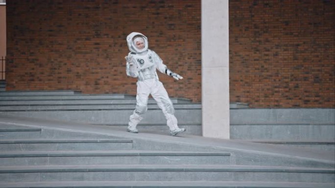 穿着宇航服的英俊男子正在水泥楼梯上跳舞。宇航员很高兴，并做出创造性的舞蹈动作。成功的太空人穿着白色的