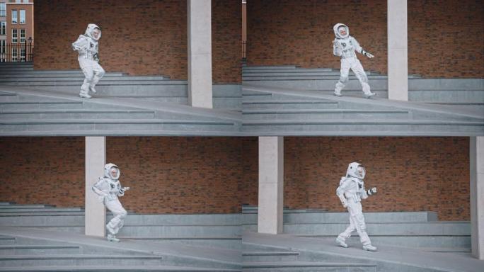 穿着宇航服的英俊男子正在水泥楼梯上跳舞。宇航员很高兴，并做出创造性的舞蹈动作。成功的太空人穿着白色的