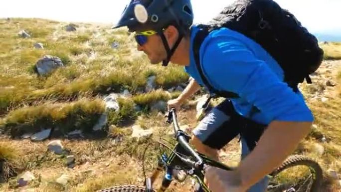男子在山高绿草的岩石自行车道上骑自行车的肖像
