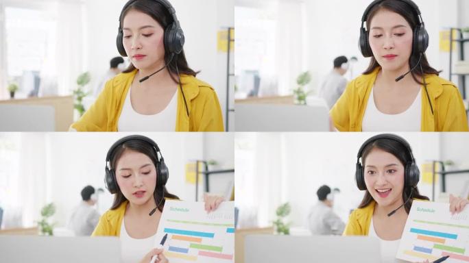 亚洲女商人在新的正常情况下进行社交距离，以预防病毒，同时在办公室工作时使用笔记本电脑向同事介绍有关视