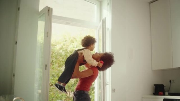 快乐的母亲抱着可爱的男婴，在现代家庭客厅玩耍，玩耍。黑人女性举起并将蹒跚学步的孩子扔向空中。童年、新
