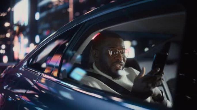 时髦的戴眼镜的黑人在晚上坐出租车的后座上下班。英俊的男性在带有工作霓虹灯的城市街道上的转车上，在智能
