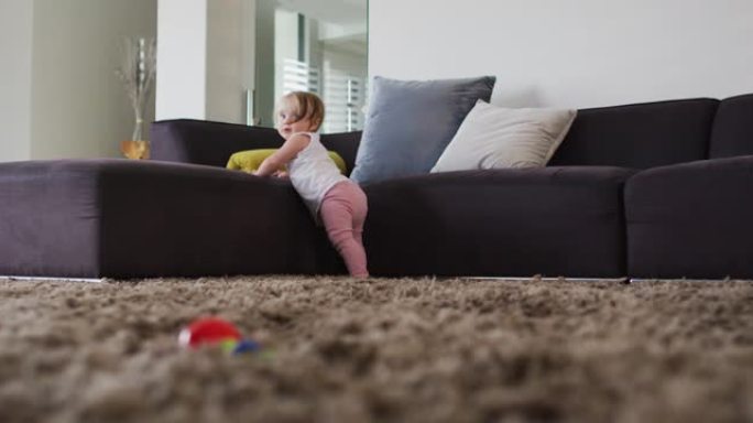 可爱的高加索婴儿站在家里拿着沙发