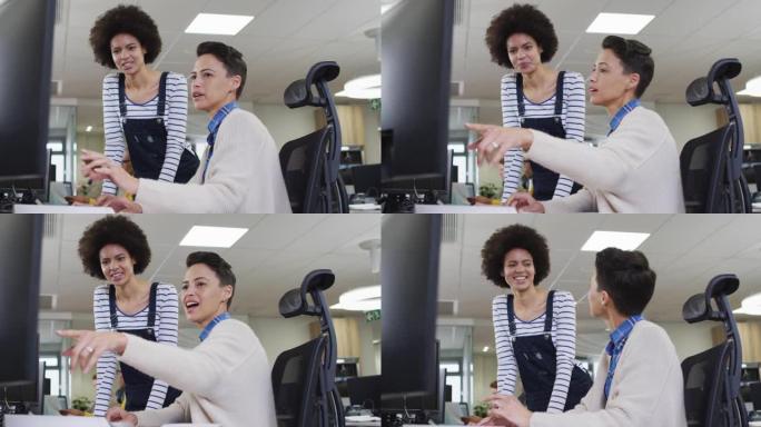 多元化的微笑女商业同事指着电脑，在办公室讨论