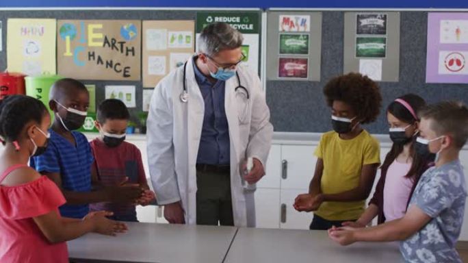 多元化的学校老师和学童站着消毒手，都戴着口罩