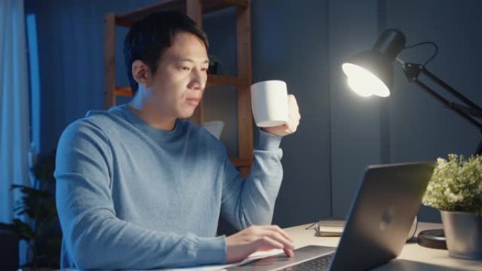亚洲商人休息一下，喝杯咖啡放松一下，晚上加班在笔记本电脑上检查工作任务，以安排在客厅的日程。