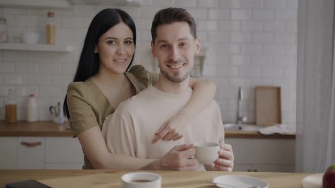 丈夫和妻子一起站在厨房里的慢动作肖像，拿着咖啡杯，微笑着