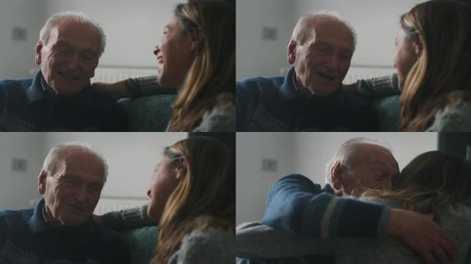电影拍摄的高级白发祖父和孙女坐在家里的沙发上，一起玩乐，深情地拥抱。概念: 生活，祖父母，世代，爱，