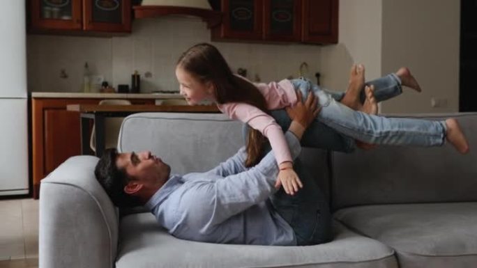 可爱的继父躺在沙发上与6岁的小女儿玩耍
