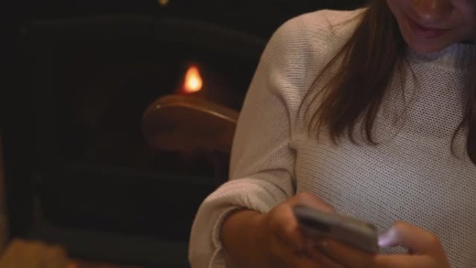 女人在家在壁炉旁的椅子上放松时使用手机