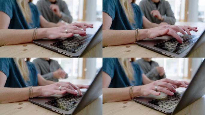 一位女商人在笔记本电脑上工作的特写镜头，同事坐在办公桌旁
