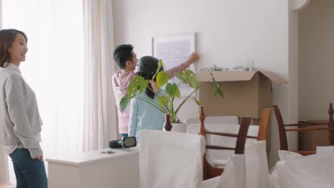 快乐的亚洲家庭搬进新房业主悬挂图片装饰房子与儿童年轻夫妇一起享受房地产投资与儿童4k镜头