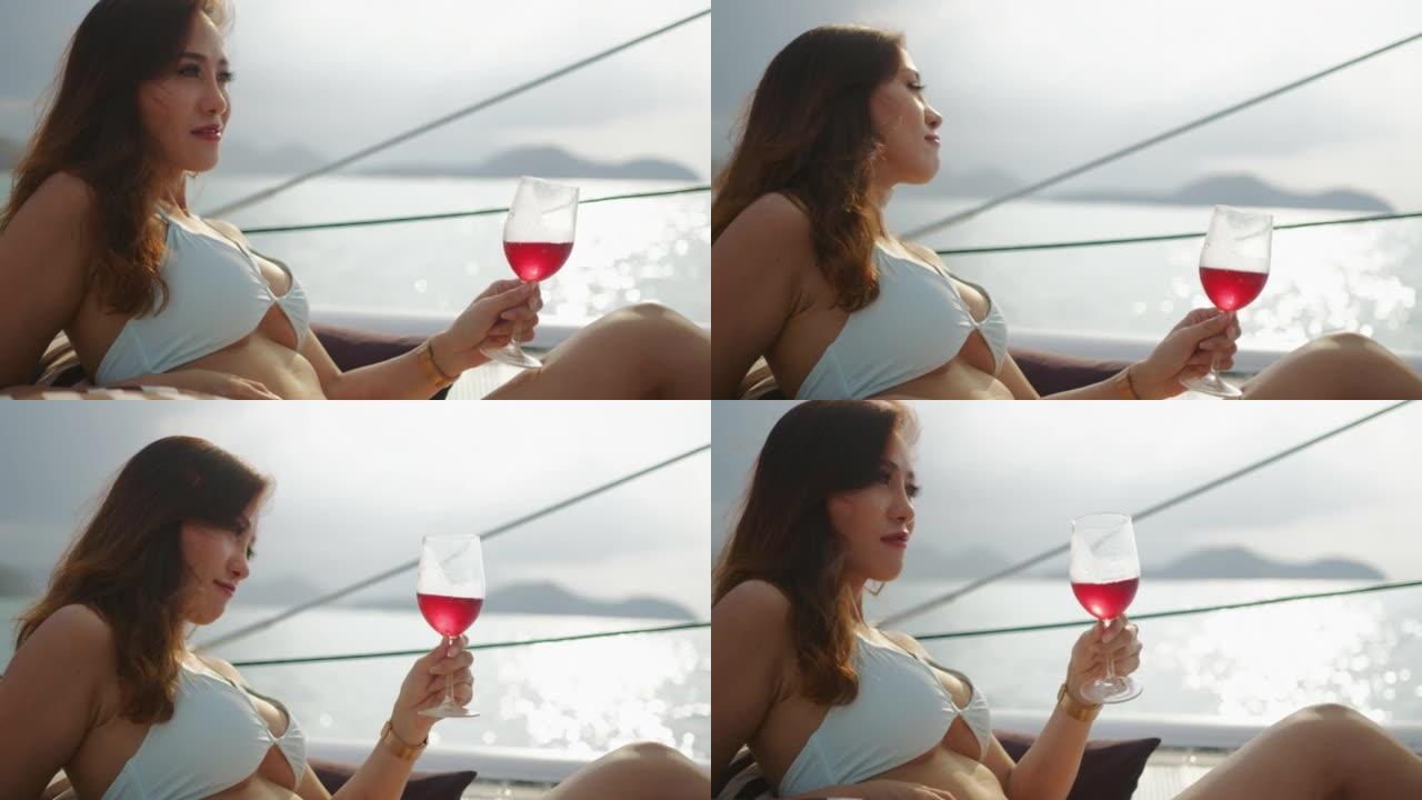 美丽的女人在日落时在游艇上放松，拿着酒杯喝酒