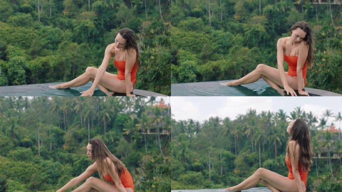 美丽的女人在游泳池边放松，穿着比基尼用手触摸水，享受在热带酒店度假度假放松，可以看到丛林天堂
