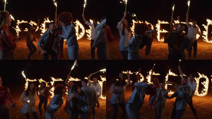 一群年轻，无忧无虑，快乐的多民族朋友玩得开心，与烟火一起跳跃和跳舞，并以烟火火字母拼写自由为背景。充