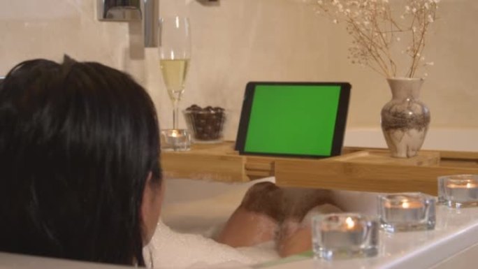 特写: 放松的年轻女士在泡泡浴中放松并观看在线视频