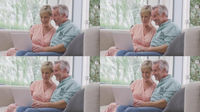 资深退休夫妇坐在家里的沙发上，用笔记本电脑进行视频通话