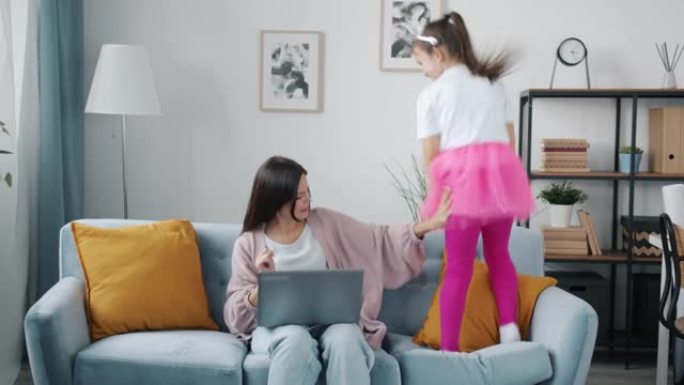 忙碌的母亲在家工作时使用笔记本电脑，而烦人的孩子则四处跳跃和奔跑