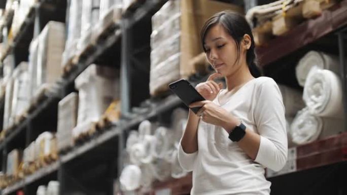 亚洲妇女在仓库和使用智能手机检查价格