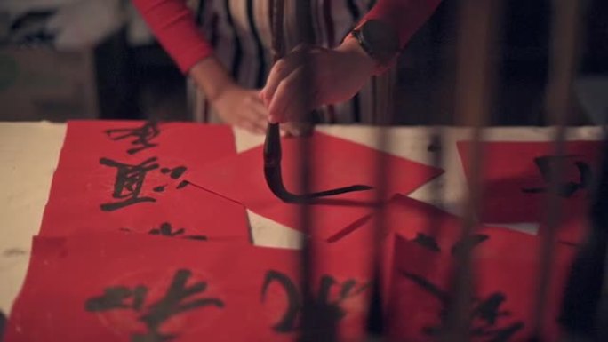 亚洲华人女性的手练习中国新年庆祝活动的到来，目的是繁荣和良好的措辞，将其写在红色的纸上