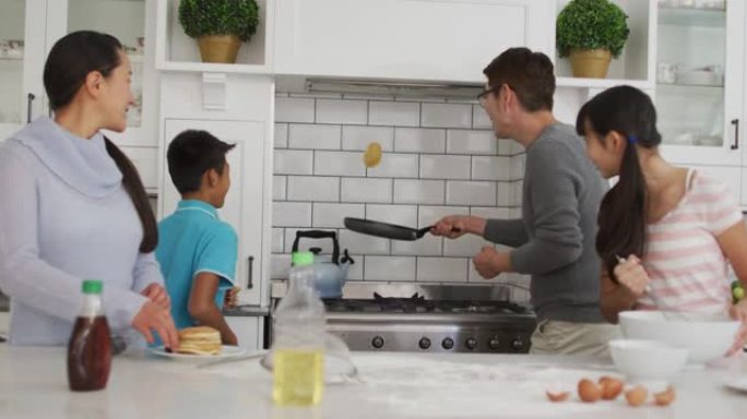 快乐的亚洲父母带着儿子和女儿在厨房里，父亲一边看一边翻煎饼