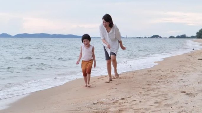 4岁的亚洲母亲和儿子的家庭在沙滩上沿着日落海浪的边缘奔跑并度过时光。家庭假期快乐。母亲节2020。轻