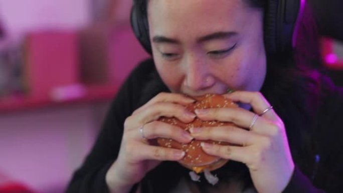 在韩国，玩游戏、吃快餐、亚洲女性一边在电脑上玩在线游戏，一边吃汉堡和薯条。游戏女孩，耳机和流媒体电子