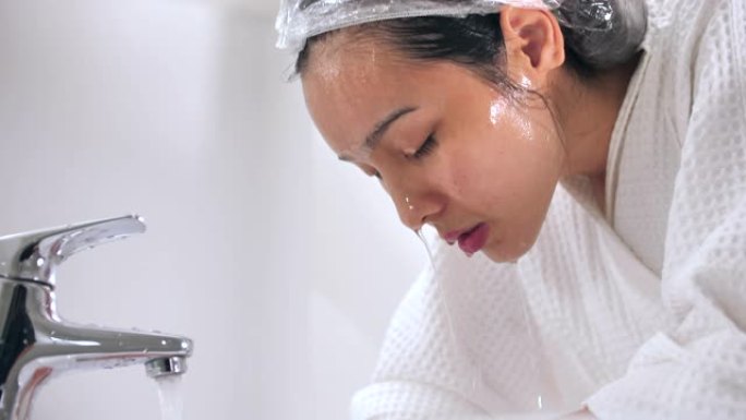 年轻的亚洲妇女在家里的浴室洗脸