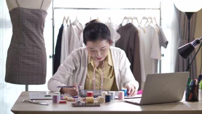 女设计师使用笔记本电脑在服装店工作。时装设计师在纸上勾勒出轮廓