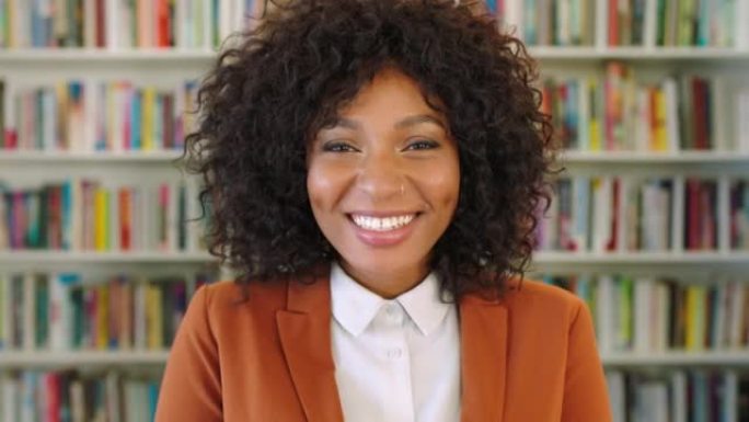 一位年轻快乐的黑人女性图书管理员对她的工作场所微笑和嘲笑。早晨学习前站在图书馆里的时尚，时尚和美丽的