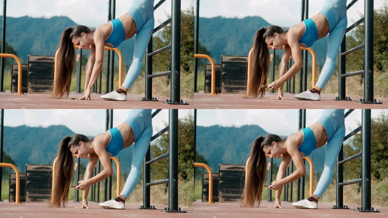 SLO MO运动女子在户外健身房伸展双腿健身时使用智能手机