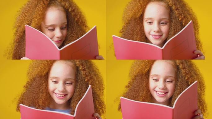 黄色背景下红头发女孩学习学校练习册的工作室镜头 -- 慢动作镜头